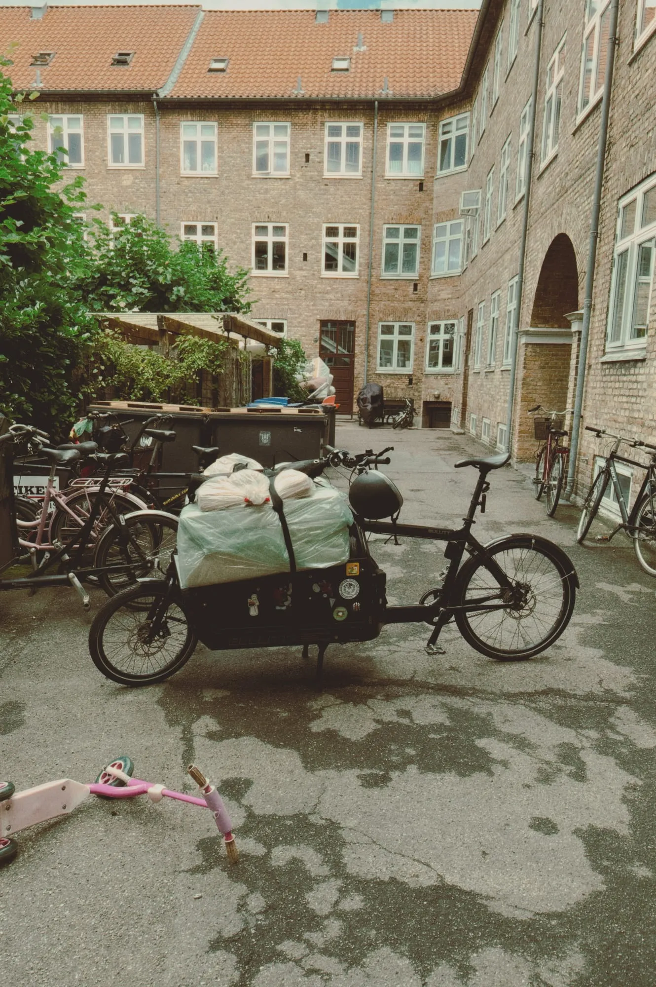 A loaded black Bullitt on its stand in a brick apartment courtyard full of bicycles.