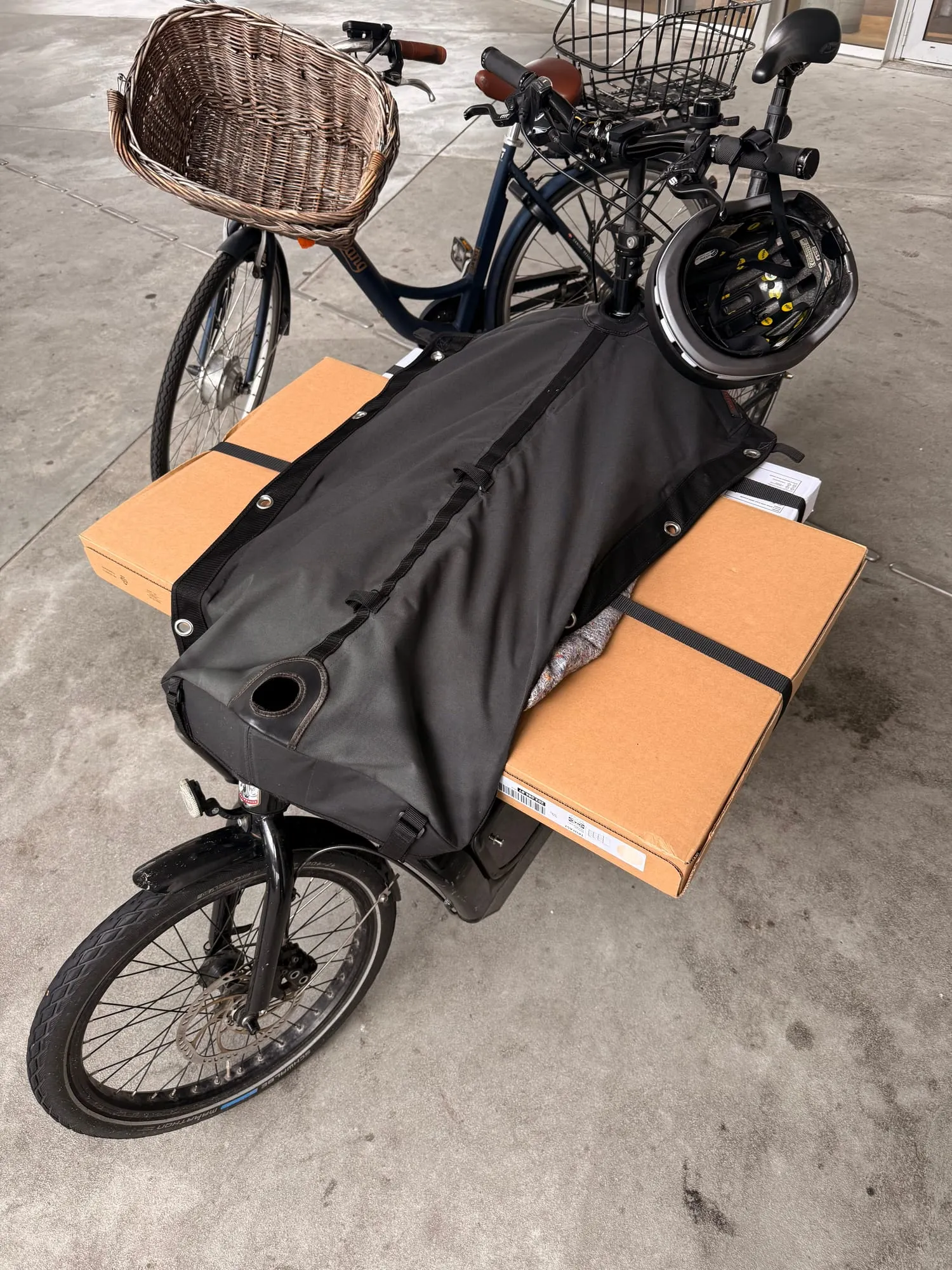 Cardboard flat-pack boxes strapped into the cargo bag of a bike, a helmet hanging from the handlebars.