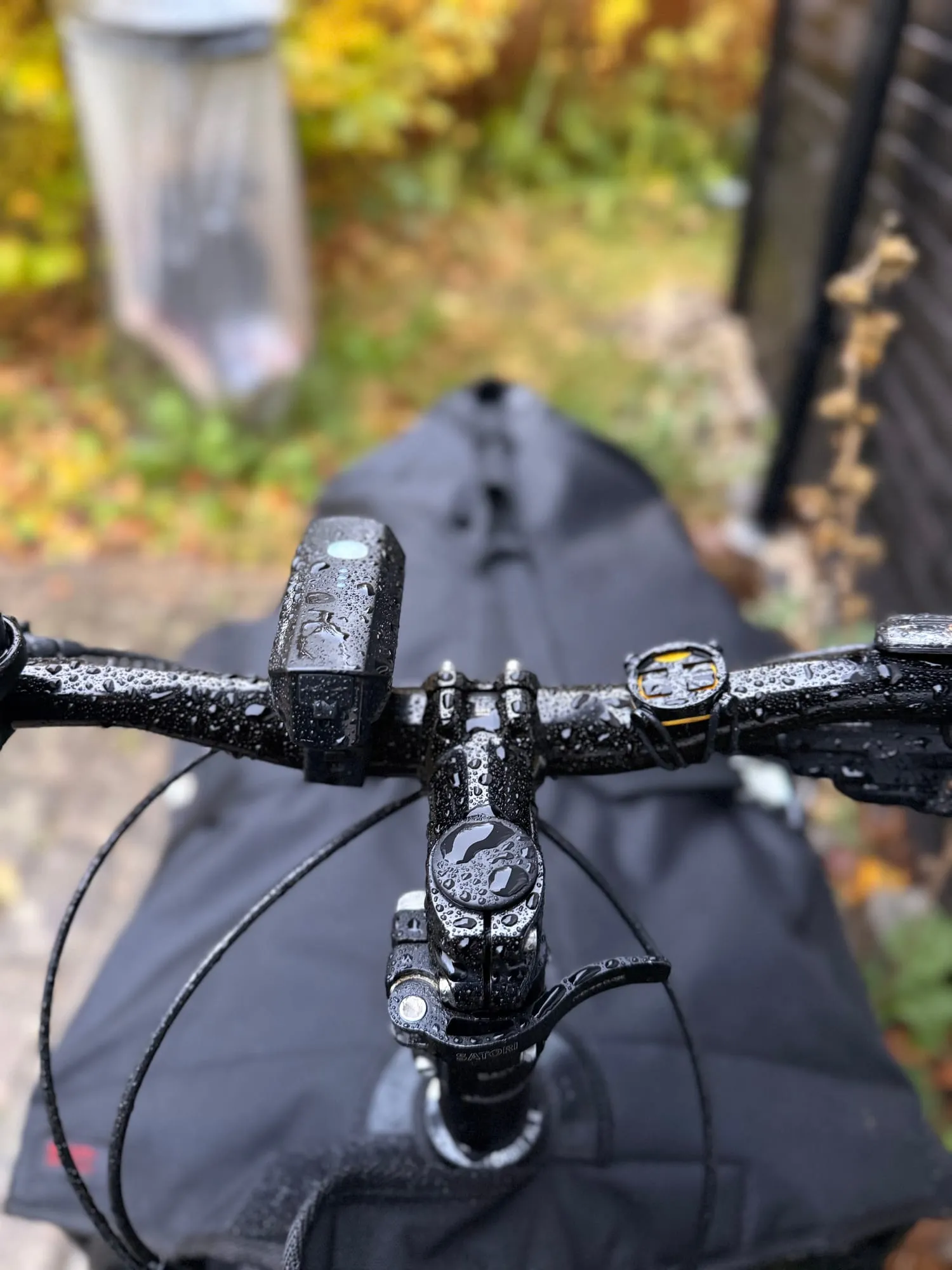 Rain-beaded black handlebars and stem, autumn foliage blurred behind.